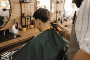 A barber trimming the neckline of a male customer’s hair using an electric hair clipper.