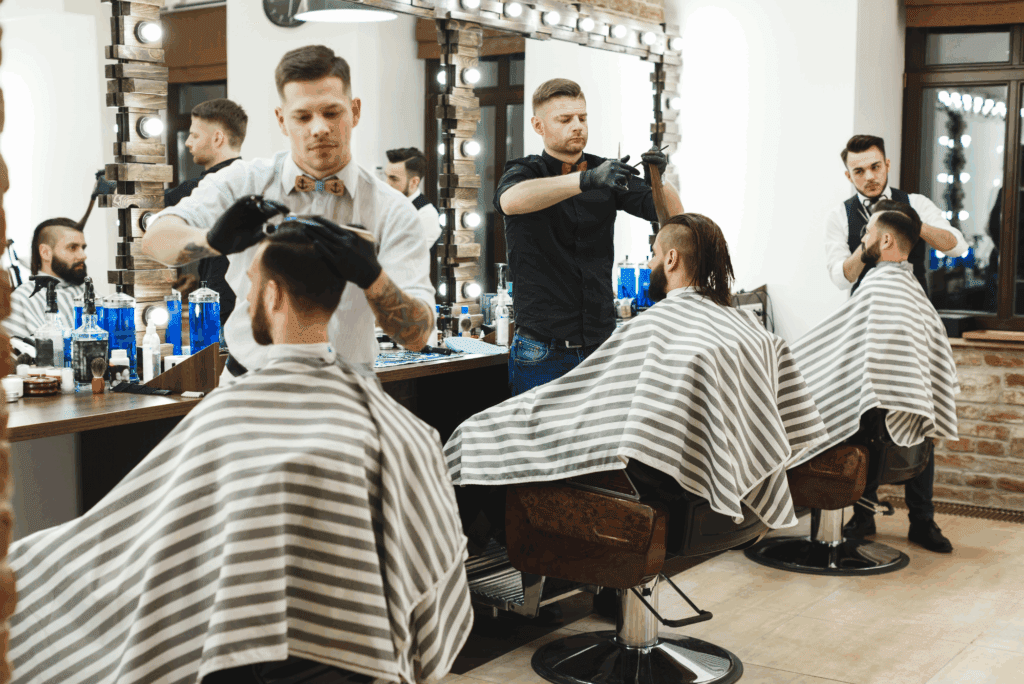 Group of well-groomed male barber students in matching striped capes receiving hands-on training in modern barbering techniques.
