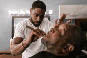Skilled barber carefully shaping client's beard with razor in professional barbershop setting.