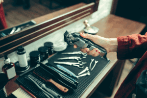 Close-up of barber’s hands skillfully handling professional clippers and scissors on color-coordinated mat.