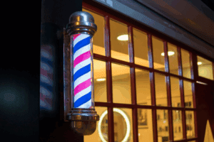 Illuminated red, white, and blue barber pole mounted on modern window.