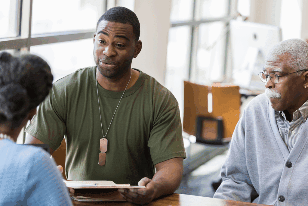 Male veteran listens intently to older black male mentor’s guidance in office setting.