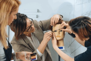 Three women students collaborating to style a mannequin head.