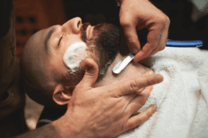 Close-up of barber carefully shaving male client’s face.
